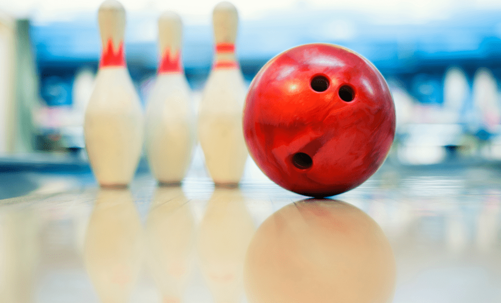 A red bowling ball and three white bowling pins sit on a clean bowling lane.