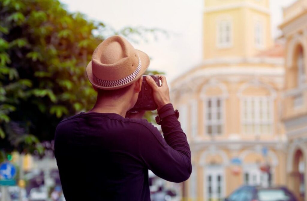 Man wearing a hat taking a photo of a building.