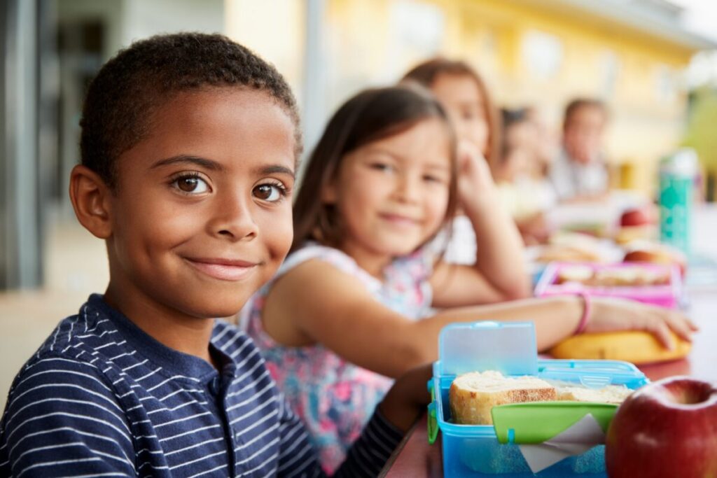 Young boy and girl at school lunch table smiling to camera.