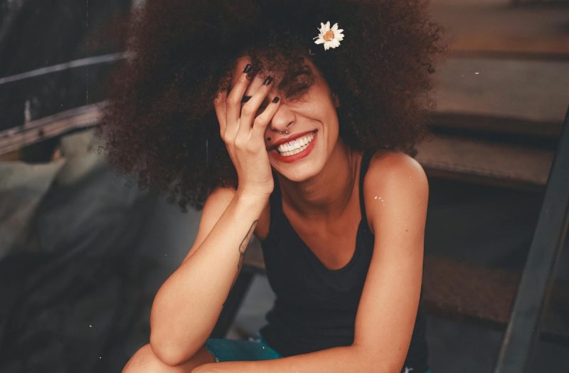 Young black woman smiling and covering part of her face.