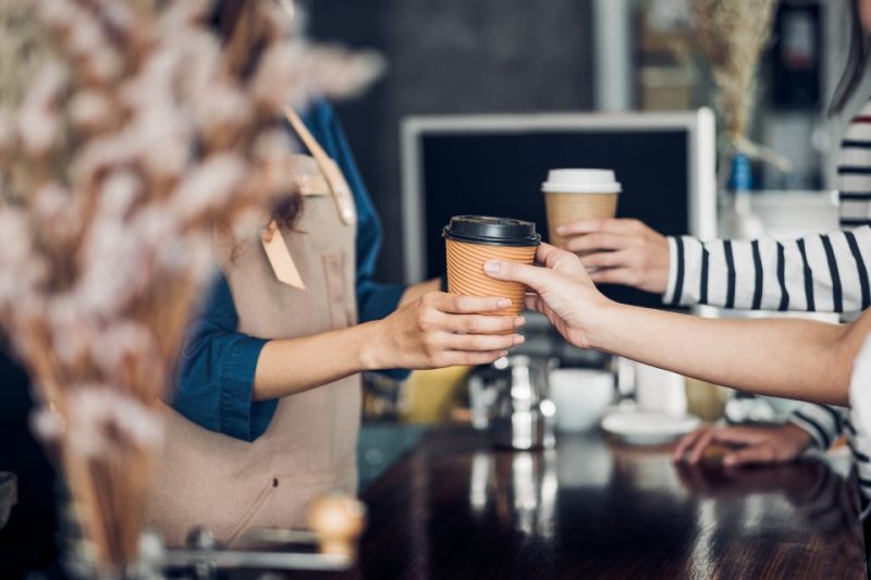 A barista handing coffees to customers.