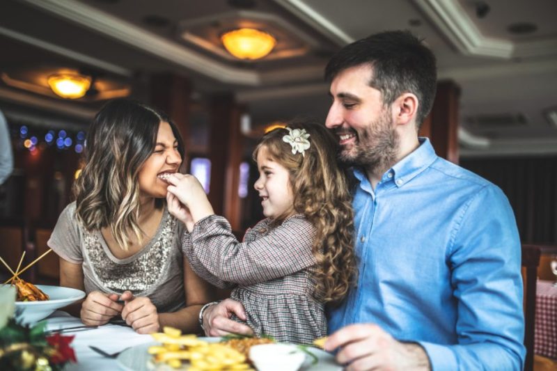 A mom, dad, and little girl happily eating at a family-friendly restaurant
