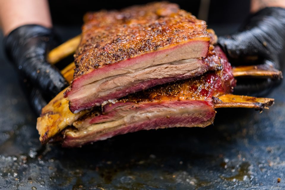 Gloved hands holding a rack of smoked ribs.