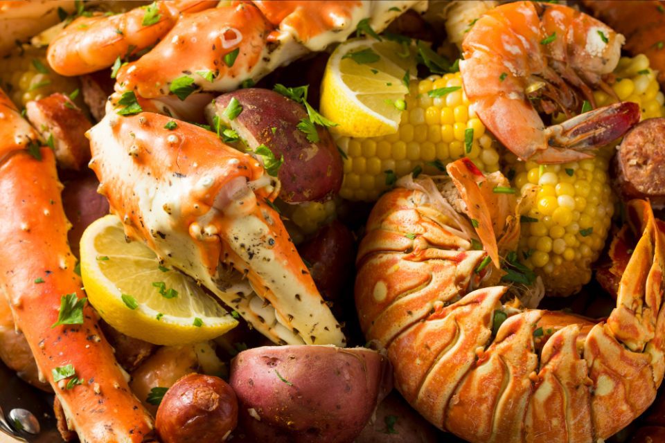 A closeup of lobster, crab legs, corn on the cob, and shrimp with lemons.