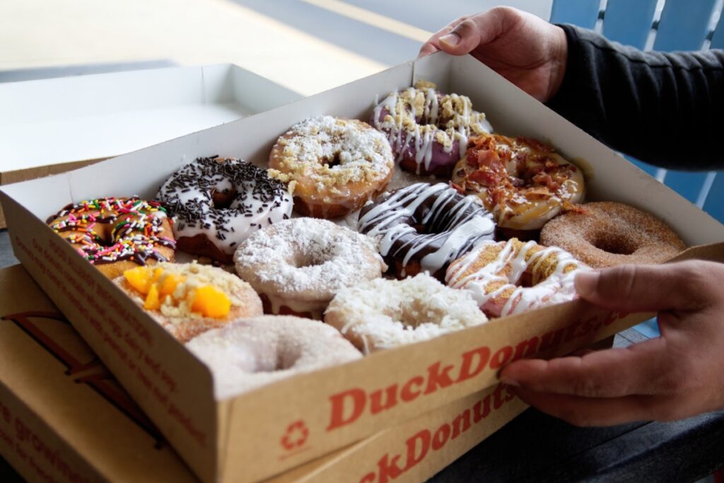 Outer Banks NC, USA 05-26-2022: A cardboard box of a dozen donuts bought from the chain store Duck Donuts. A popular selection of assorted donuts are made to order fresh.