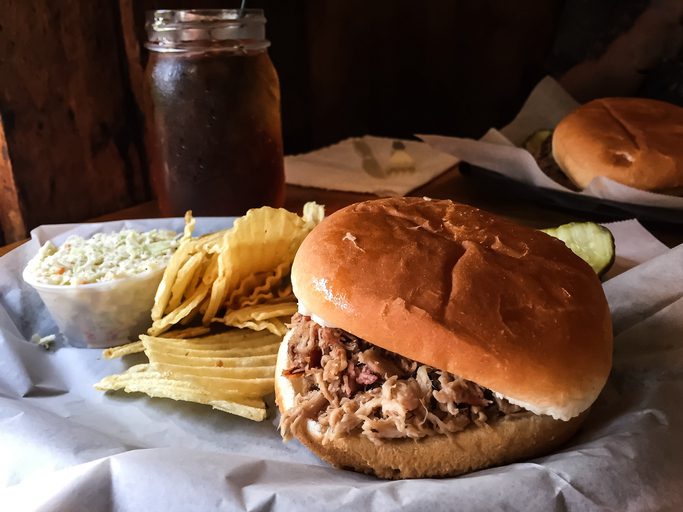 A meal of pulled pork BBQ, potato chips, cole slaw, and sweet tea in a mason jar. A North Carolina southern meal.