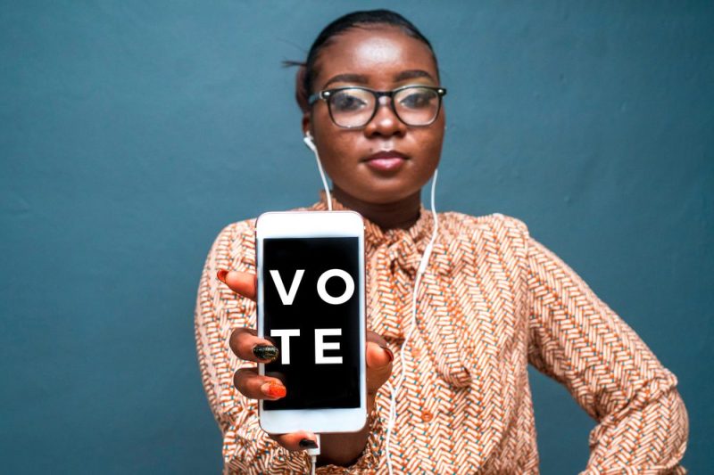 Woman holds up a phone that says "vote."