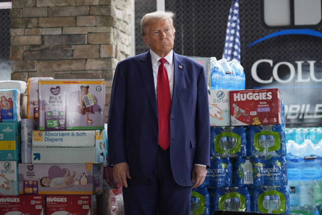 Republican presidential nominee former President Donald Trump listens as Georgia Gov. Brian Kemp speaks at a temporary relief shelter as he visits areas impacted by Hurricane Helene, Friday, Oct. 4, 2024, in Evans, Ga. (AP Photo/Evan Vucci)