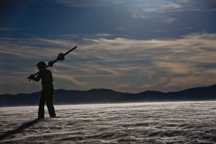 A silhouetted man stands holding his skis over his shoulder on the snow covered area of North Carolina.