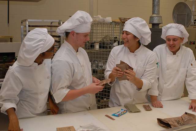 Student chefs smiling and working in the kitchen.
