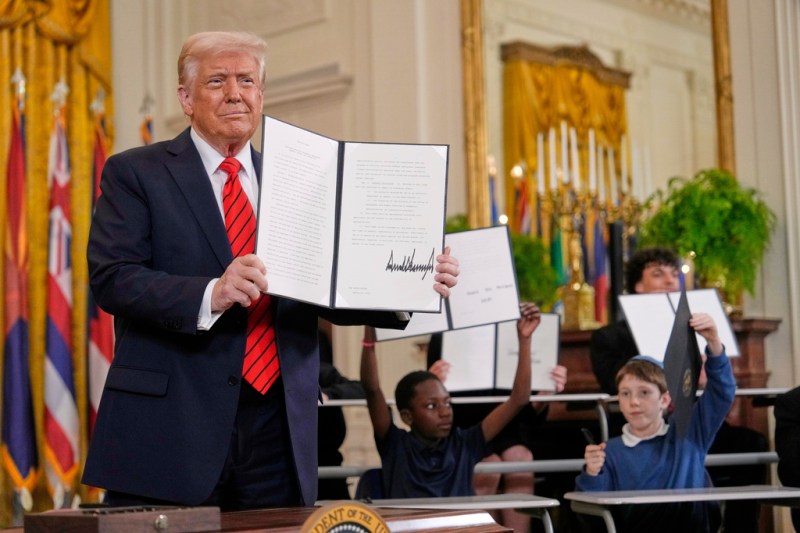 Photo of President Donald Trump, left, holds up a signed executive order as young people hold up copies of the executive order they signed at an education event in the East Room of the White House in Washington