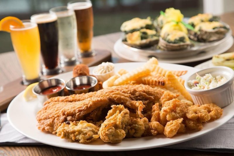 a plate of fried fish with slaw, french fries, and sauces