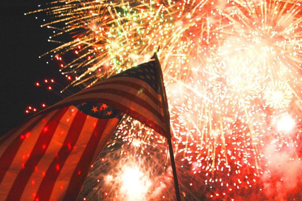 fireworks going off in the sky behind an american flag