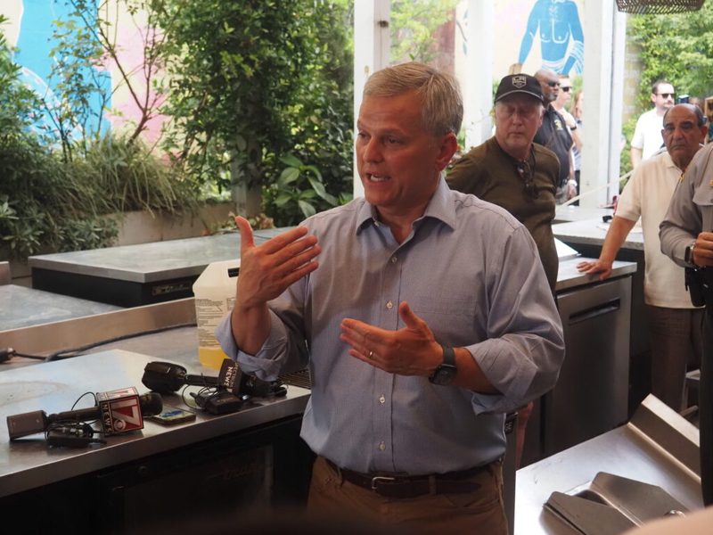 a white man with white hair in a blue shirt addresses a crowd of people
