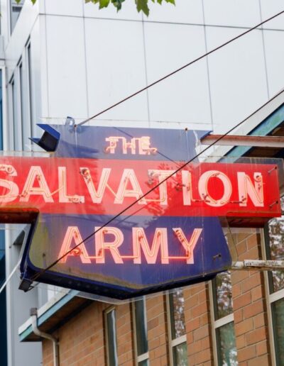 Vancouver, Canada - Sep 25,2025: Vintage neon Salvation Army sign glowing red and blue on rusty bracket above brick facade