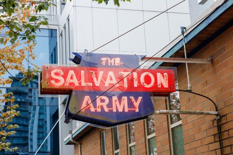 Vancouver, Canada - Sep 25,2025: Vintage neon Salvation Army sign glowing red and blue on rusty bracket above brick facade