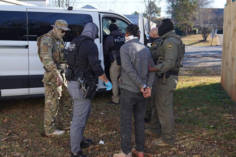Photo of federal immigration agents blindfolding and arresting a man.