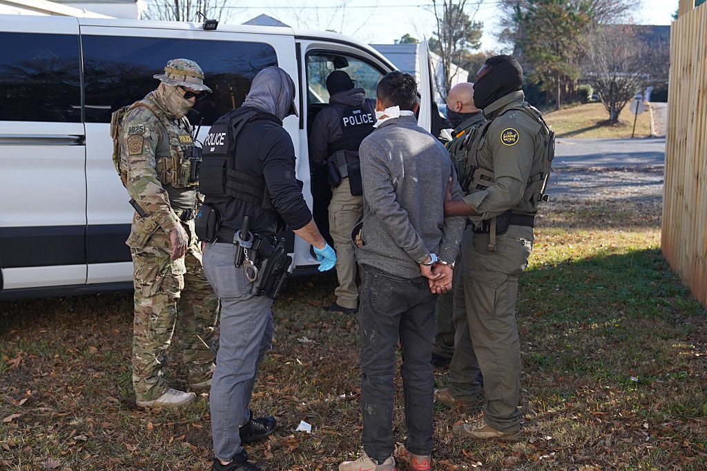 Photo of federal immigration agents blindfolding and arresting a man.