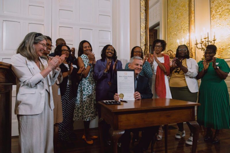 Photo of Gov. Josh Stein posing with the signed proclamation recognizing April 11-17 as Black Maternal Health Week. Behind him stand several advocates including NC Senator Natalie Murdock.