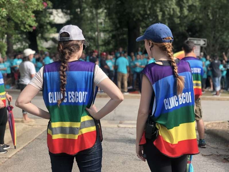 Photo of two women wearing rainbow-colored vests, working as abortion clinic escorts