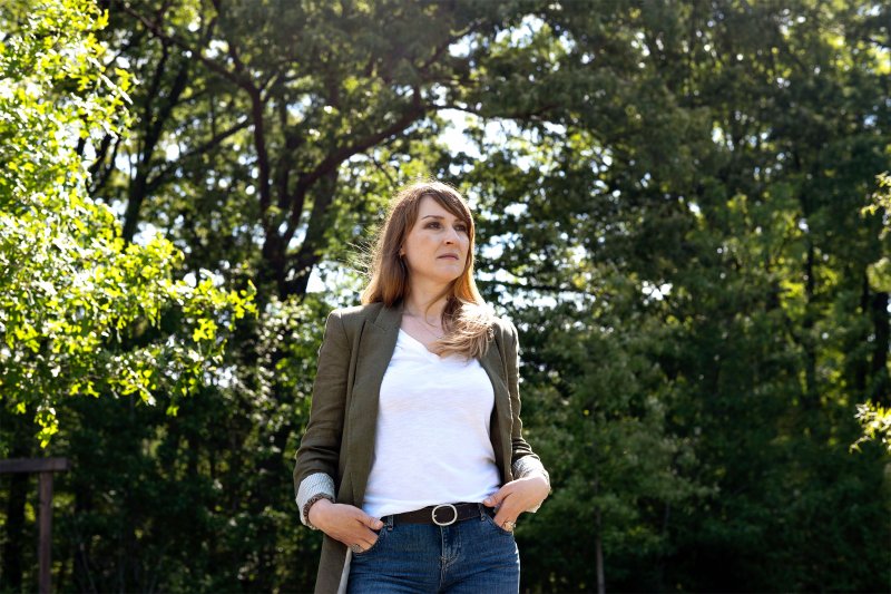 Photo of a woman posing for the camera, looking away outside in front of trees.